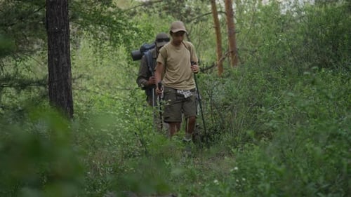 Polyethnic Father and Son with Backpacks Marching through Green Forest