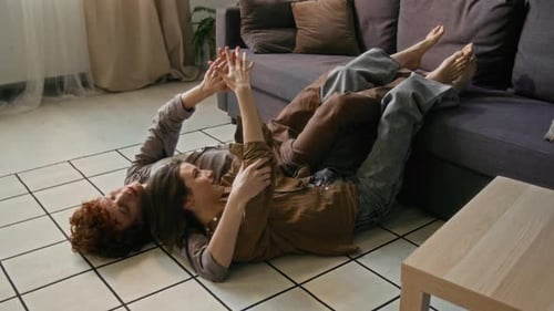 Man Lying on Floor with his Smiling Girlfriend Playfully Draped Over Him