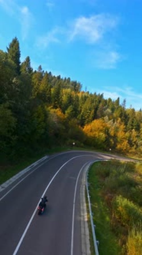 Aerial Views of Professional Biker Riding Motorcycle Along Road in Beautiful Forest Landscape Motion
