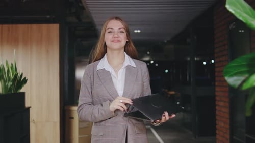 A Professional Woman Confidently Stands in a Modern Office Environment Holding a Laptop Embodying