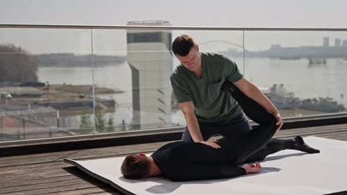 Male Physiotherapist Providing Handson Stretching Assistance to Men Patient on a Bright City Rooftop