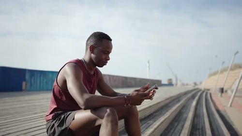 Athletic Man Sits on Steps Using Cellphone and Smiles