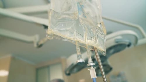 Drop counter transparent bag for medicine. Close up. Modern surgery room at backdrop in blur.