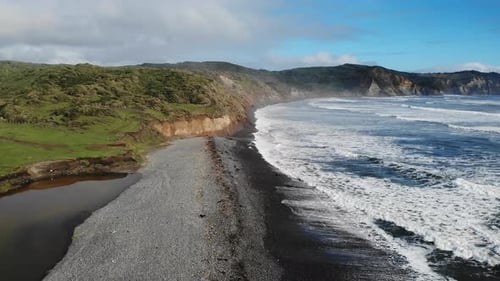 Ocean Waves Crashing on a Black Sand Beach Below Green Cliffs