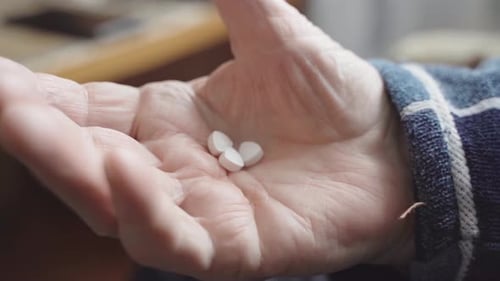 Close Up View of Senior Male Hand Holding Two Pills While Feeling Bad and Taking Treatment