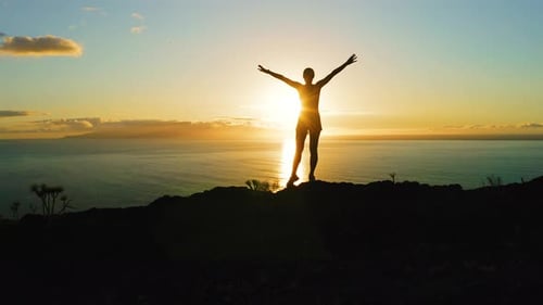 Young Inspired Woman Raises Her Hands Up Standing on the Top of a Mountain Above the Sea Against