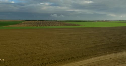 Aerial farmland reveal with a plowed field and cloudy sky.