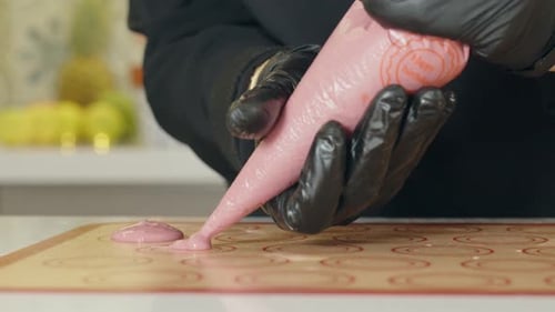 Chef pâtissier en gants noirs versant du rose fondu sur le plateau à l'aide d'une poche à douille. gros plan