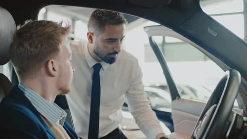 Man Sitting in New Car in Showroom and Salesman Demonstrating its Features
