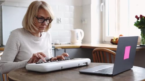 Woman Playing Keyboard at Table with Laptop