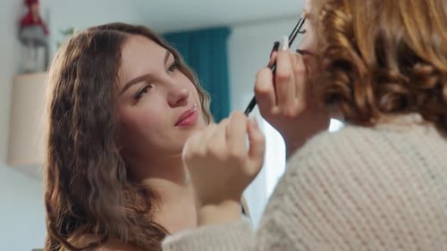 Caucasian Friends Sharing Mirror Makeup Moment Playful Blush Application Warm Apartment Light