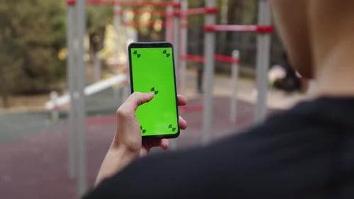 Man Using Smartphone in Hand with the Mockup Green Screen Doing Swipe Scrolling Gestures Standing on