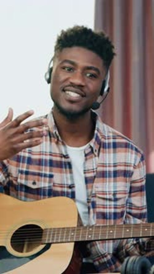 Man with guitar and headset talking to camera