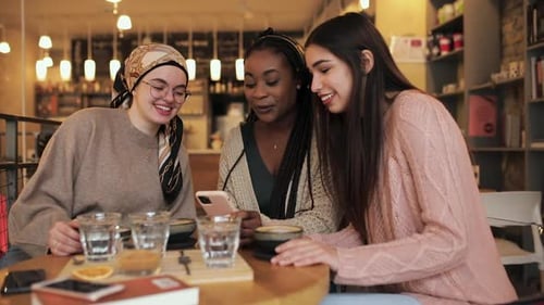 Three young multiethnic female friends spending time together at a coffee shop.
