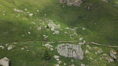 Aerial shot of a mountain biker navigating a narrow rocky trail through a alpine landscape, surround
