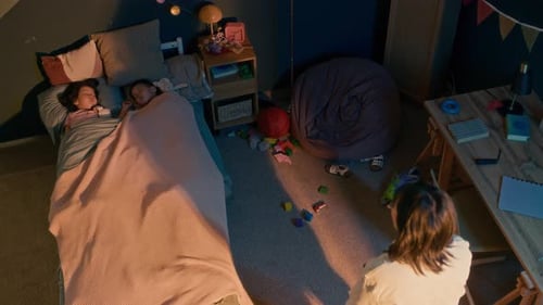 Mother Tucking In Sleeping Children in Bedroom at Night