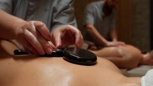Scène de massothérapie relaxante pour couples aux pierres chaudes avec gros plan des mains du thérapeute placées en douceur