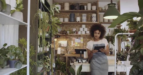 Young adult female small business owner working on digital tablet in store doing finance admin