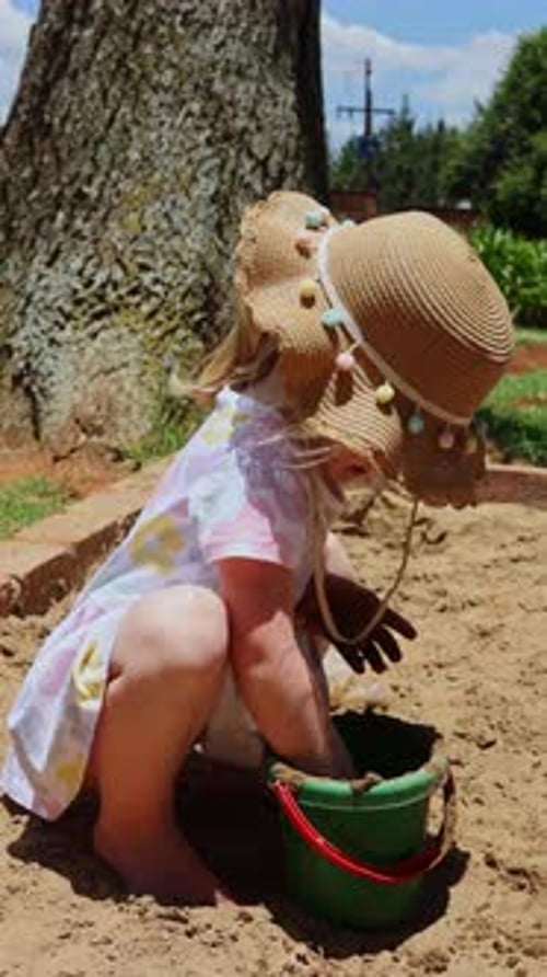 Vertical shot of little blonde girl playing with mud in sandbox at playground making mud pies.