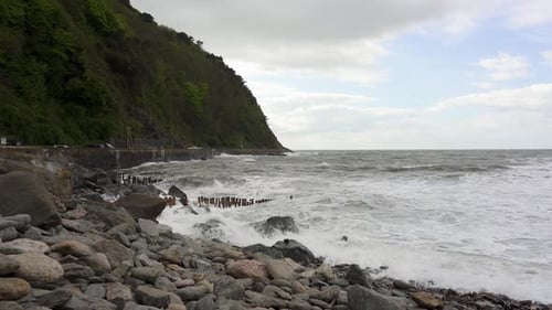 Frothy waves crash agianst the rocky beach and sea defences in Lynmouth on a very windy day. Devon,