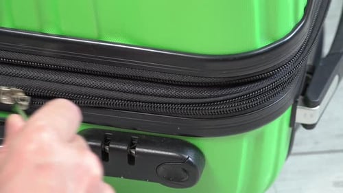 Guy opens and closes green baggage case with clothes in hand luggage zip up zipper. Man packing