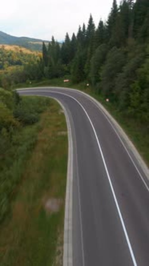 Fliegende FPV-Drohne über eine wunderschöne Landstraße im malerischen Tal, im sommergrünen Wald