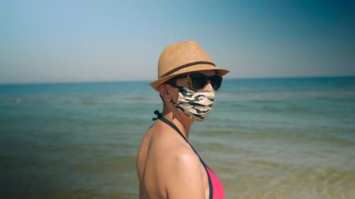 Back of a beautiful woman at the beach wearing a protective face mask