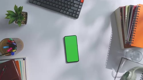 Top down view of a mock up green screen smartphone on a white office desk