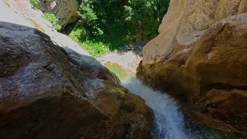 Aerial Video of a Scenic Waterfall Cascading Down a Rocky Mountain Cliff Surrounded By Lush Green