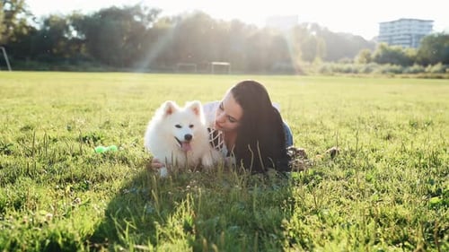 Brunette having a walk with her white dog outdoors on the field at daytime