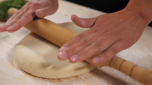 Hands Rolling Dough with Rolling Pin in Kitchen