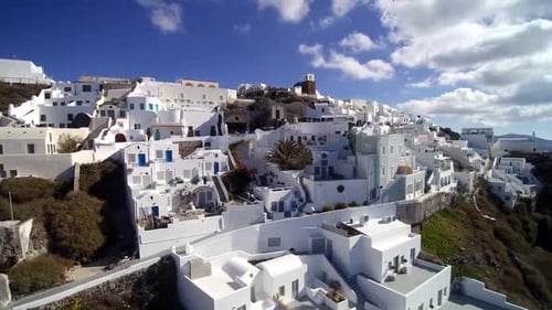 A charming view of Santorini’s white-washed buildings nestled on the hillside, with blue accents, na