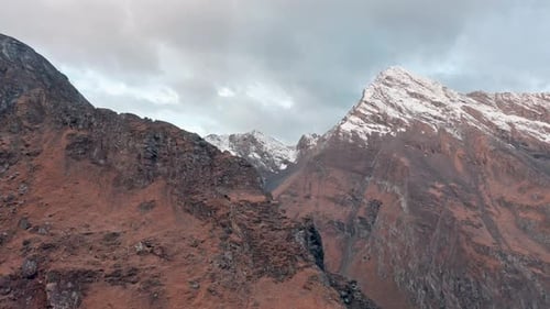 Snow-capped mountain peak with rugged terrain and reddish rocks at twilight
