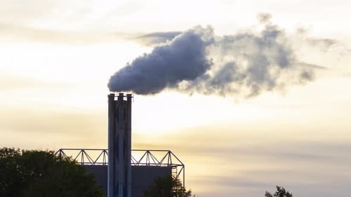 Time lapse of smoking factory chimney against the background of a setting sun - crop