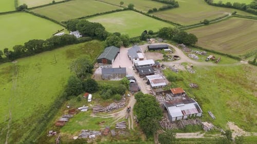 Aerial view of a smallholding lumber yard with various buildings and wood piles in a rural setting