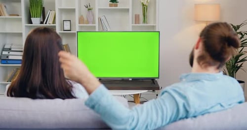 Feliz pareja viendo la televisión y cambiando de canal mirando la pantalla verde en la moderna sala de estar.
Mujer