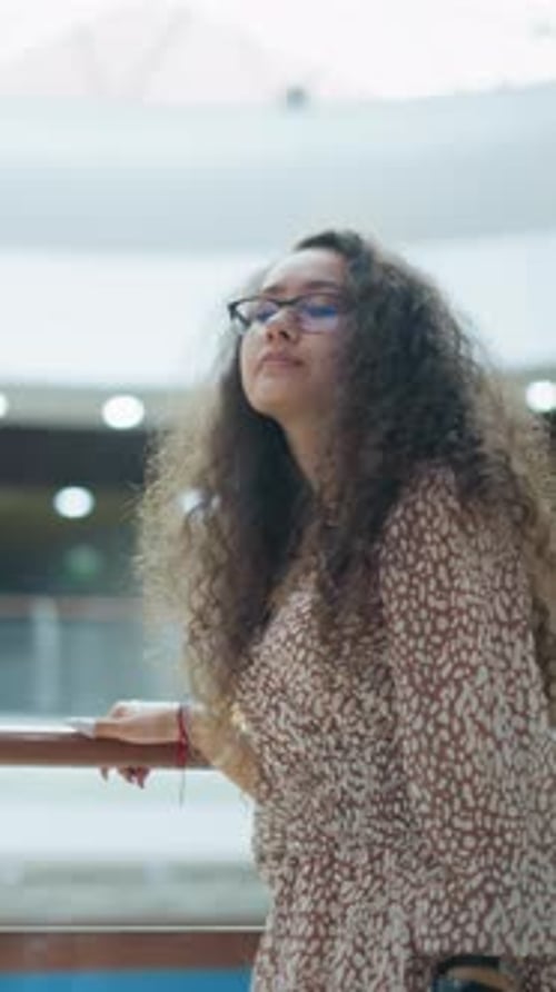 Femme en tenue vintage ajustant ses cheveux par une balustrade dans Bright Mall
