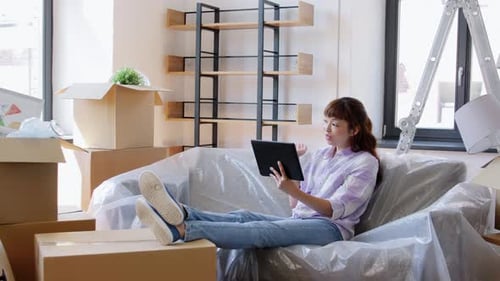 Woman video calling on tablet surrounded by boxes
