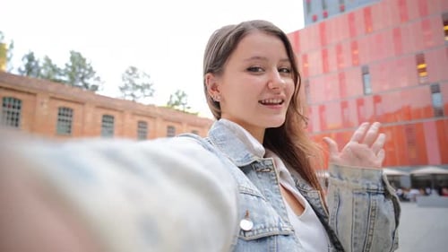 Young Woman Waving and Smiling in Urban Setting