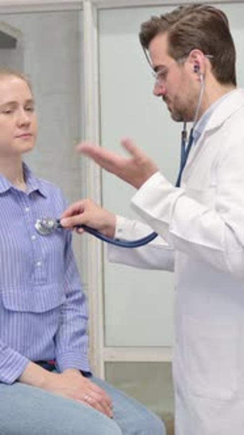 Male Doctor Uses Stethoscope on Young Woman Patient