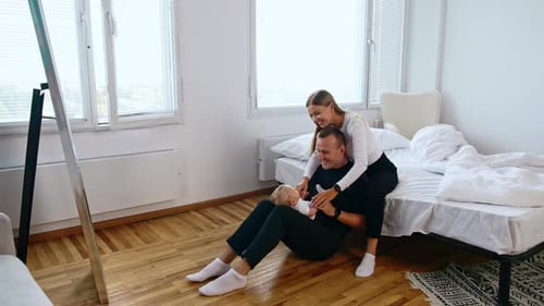 Loving dad sits on the floor with cute infant on laps. Woman sits behind her man touching the baby.
