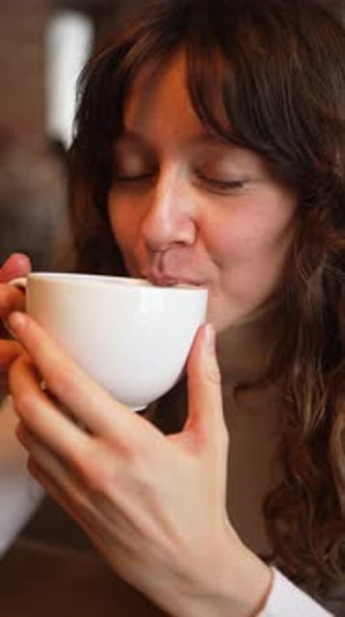 Relaxed Female Sipping Hot Drink Sitting Near Large Window Soft Daylight Illuminating Peaceful Cafe