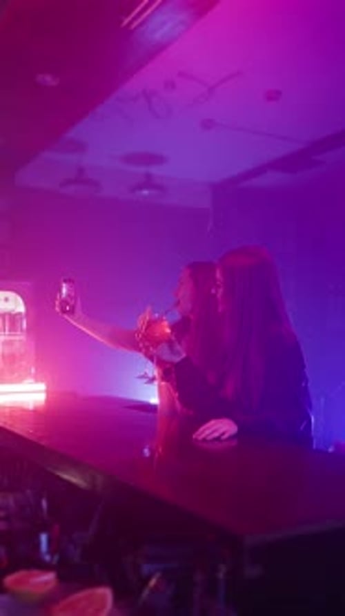Two Happy Women in a Night Bar Take a Selfie on the Phone in Neon Lighting