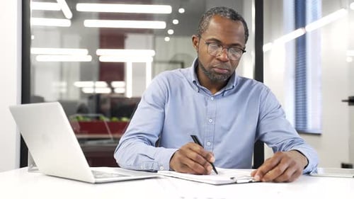 Busy african american financier is doing paperwork, fills out documents while sitting at workplace