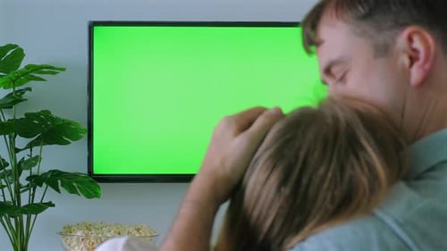 Man Embracing Child While Watching TV with Green Screen in Background