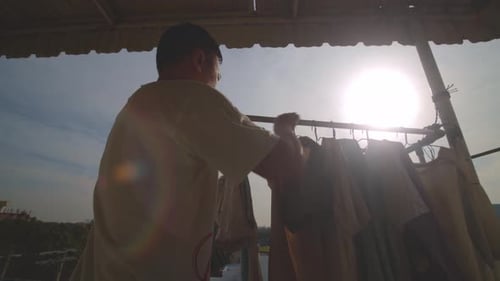 The sun shines on drying laundry on an Asian man's apartment balcony - lens flare
