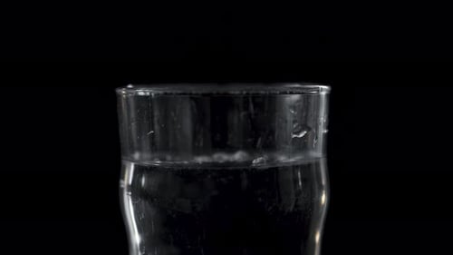 Weißes Pulver, das in ein Glas Wasser fällt und sich dann auflöst.