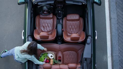 Mujer poniendo bolsas de comestibles en un convertible, vista desde arriba, mujer adulta joven colocando la bolsa de compras