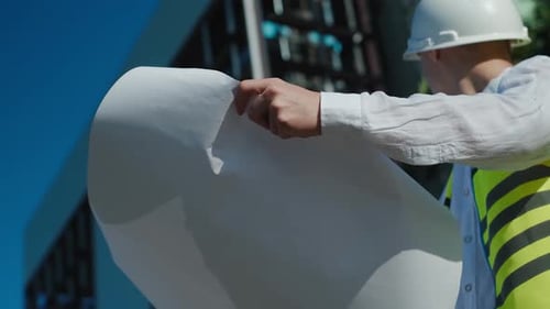ein männlicher Architekt, ein Baumeister mit einem weißen Schutzhelm und einer Arbeitsweste, schreibt Daten für den Bau auf Papier d