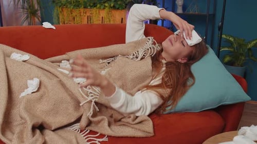 Une femme malade souffrant d'un rhume ou d'une allergie allongée sur le canapé de la maison éternue et essuie la morve dans la serviette